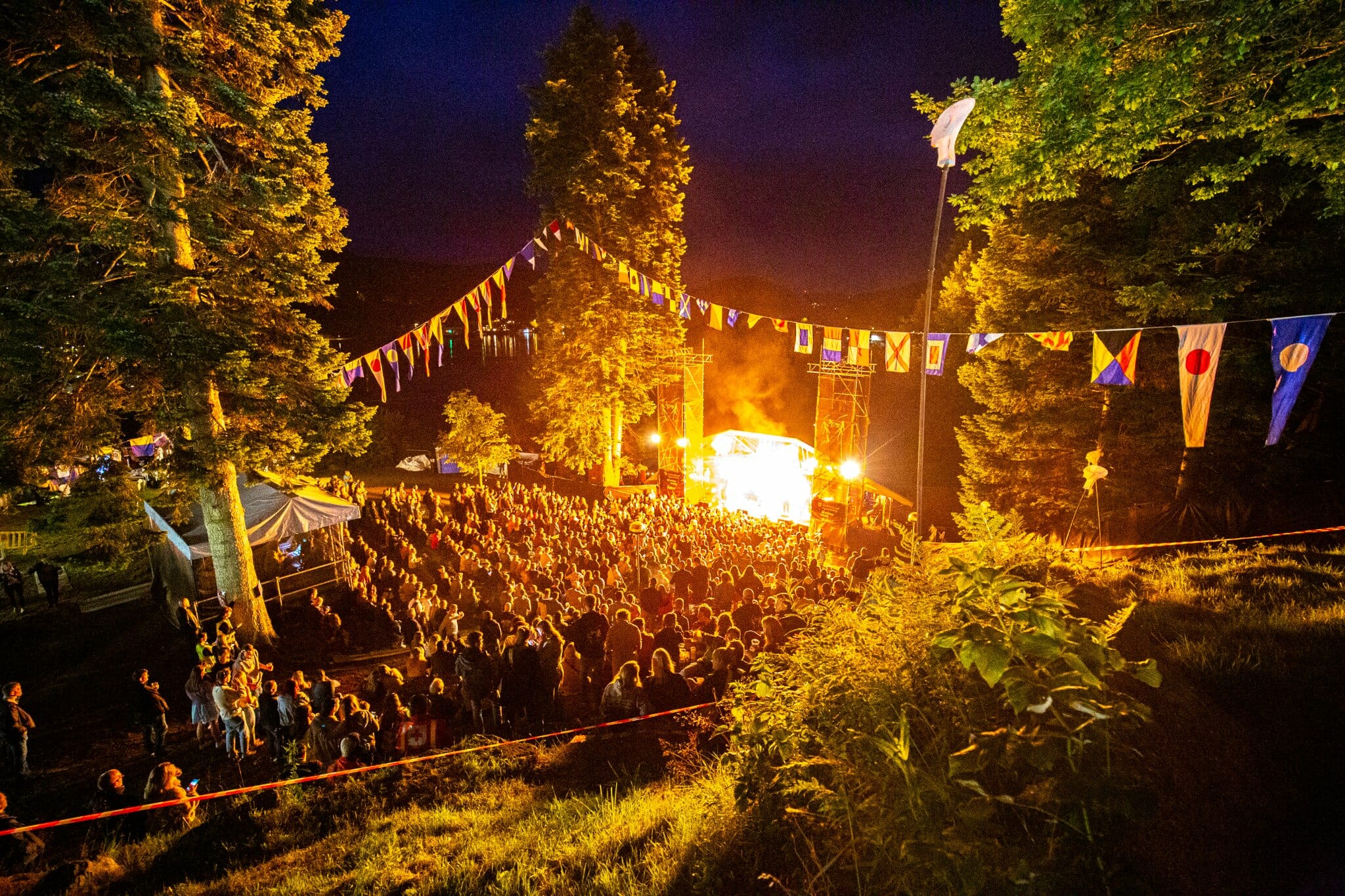 Bildet viser hovedscenen på Fjellparkfestivalen 2022. Bildet er tatt fra en skråning bakerst i publikum. Det er mye pyroeffekter på scenen. Bandet som spiller er Kvelertak.